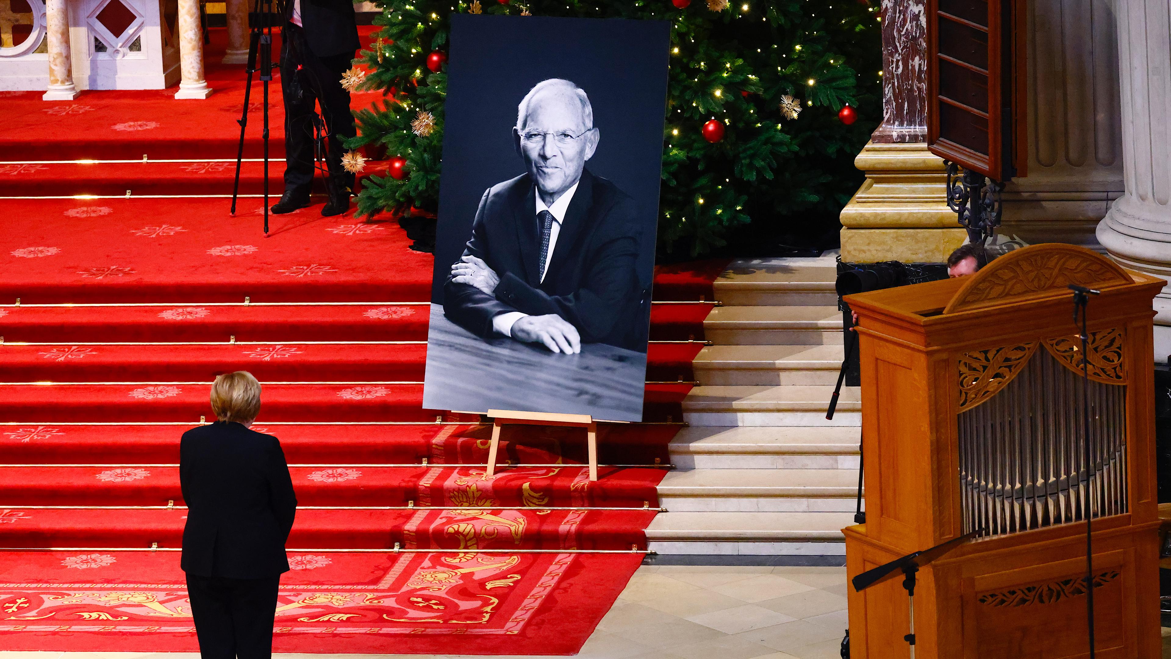 Ehemalige Bundeskanzlerin Angela Merkel steht vor einem Porträt des CDU-Politikers Wolfgang Schäuble