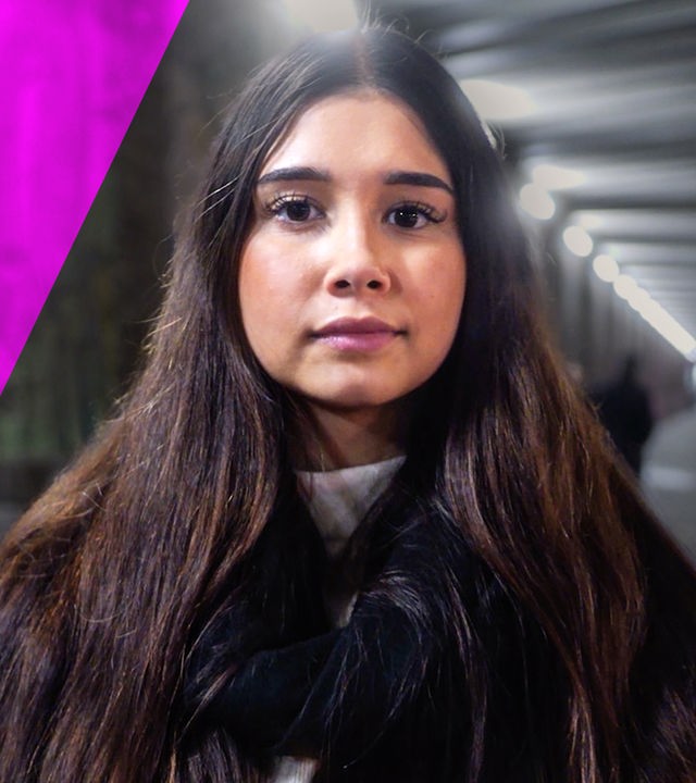 Eine junge Frau blickt ernst nach vorne. Im Hintergrund ist eine Graffiti-Wand zu sehen.