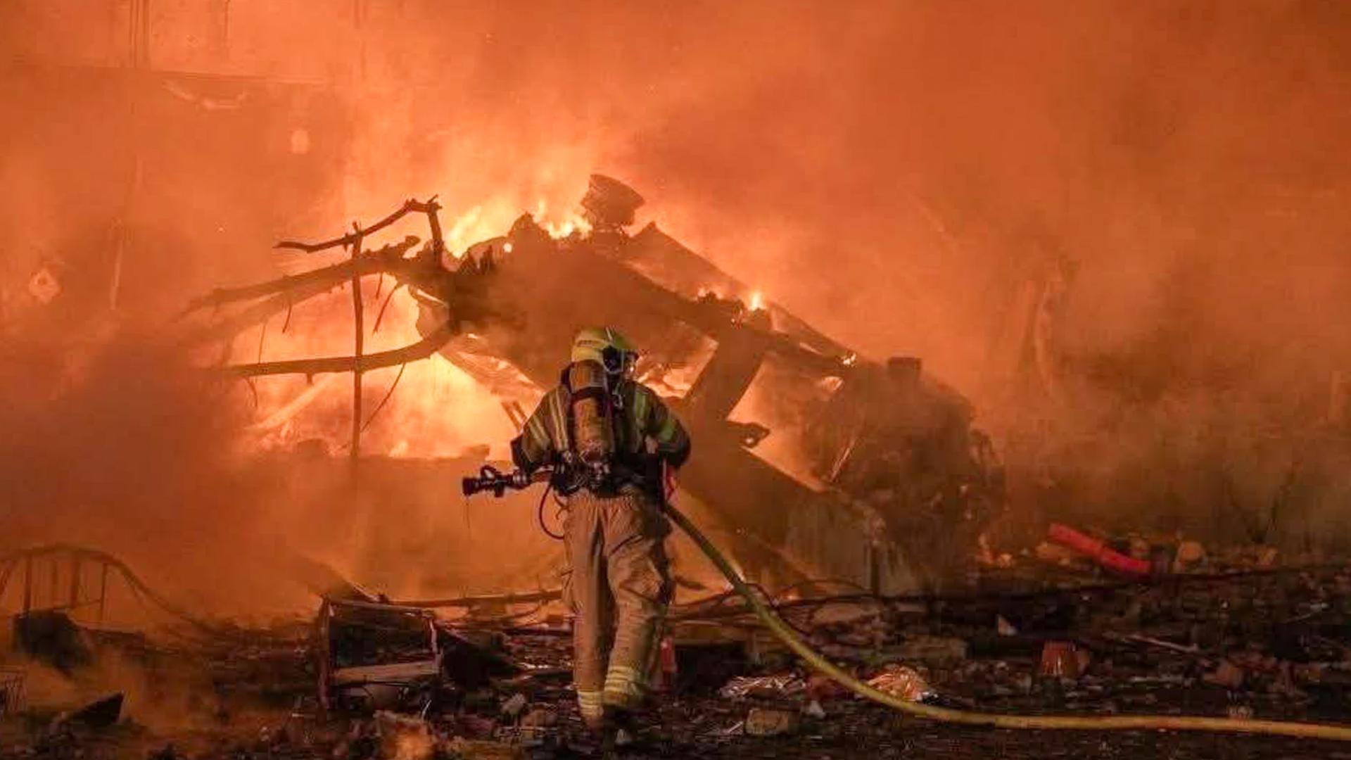 Schäden durch einen iranischen Raketenangriff inmitten einer Militäroperation der Vereinigten Staaten und Israels gegen den Iran. Es brennt sehr stark und ein Feuerwehrmann ist zu erkennen.