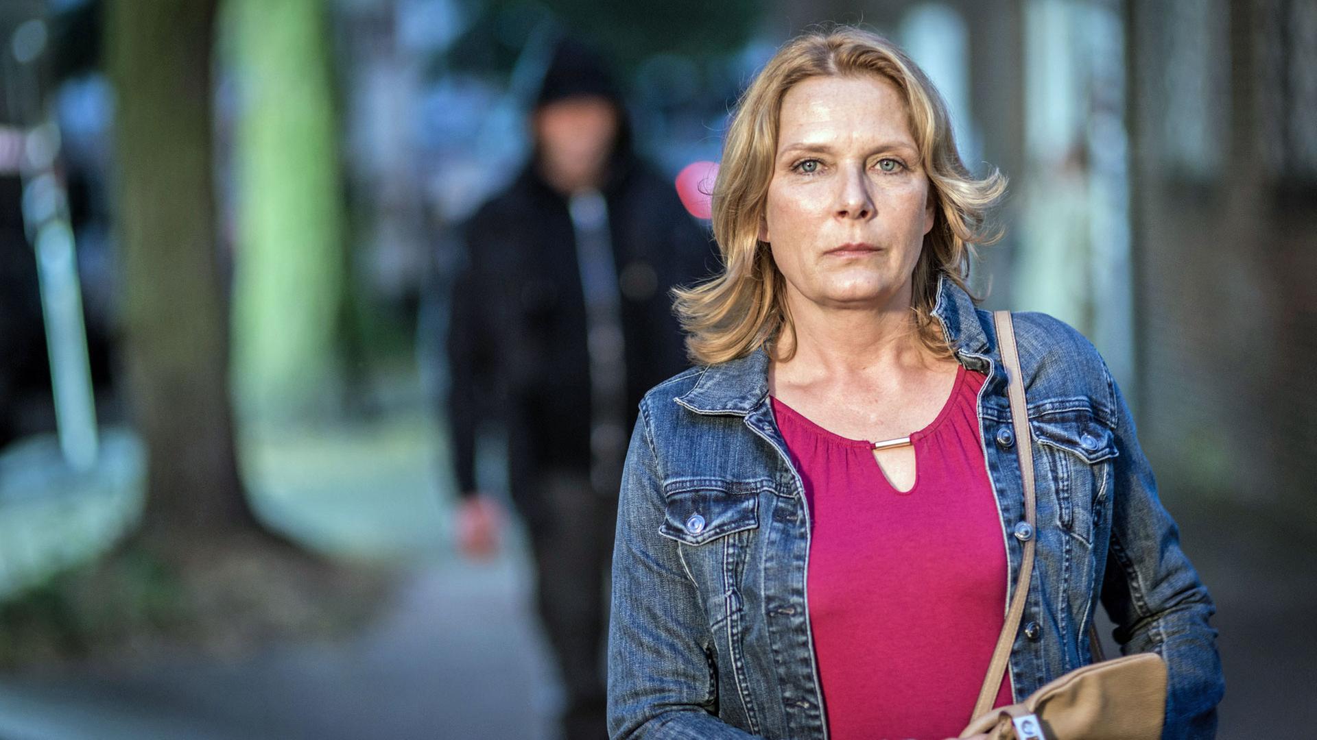 "Notruf Hafenkante - Angst": Die Polizeibeamtin Claudia Fischer (Janette Rauch) in zivil auf dem Weg nach Hause durch einen Park. Im Hintergrund ein unbekannter Mann mit Kapuze, der ihr folgt.