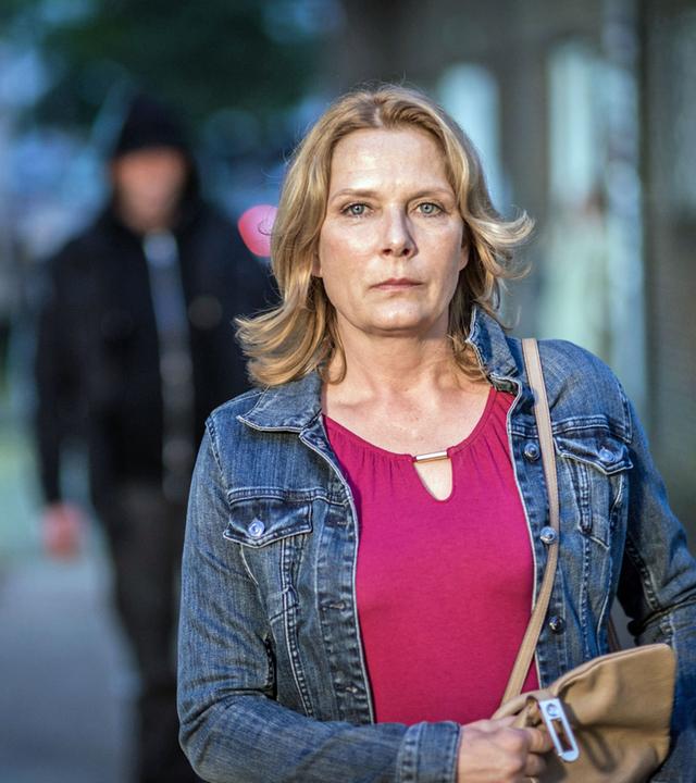 "Notruf Hafenkante - Angst": Die Polizeibeamtin Claudia Fischer (Janette Rauch) in zivil auf dem Weg nach Hause durch einen Park. Im Hintergrund ein unbekannter Mann mit Kapuze, der ihr folgt.