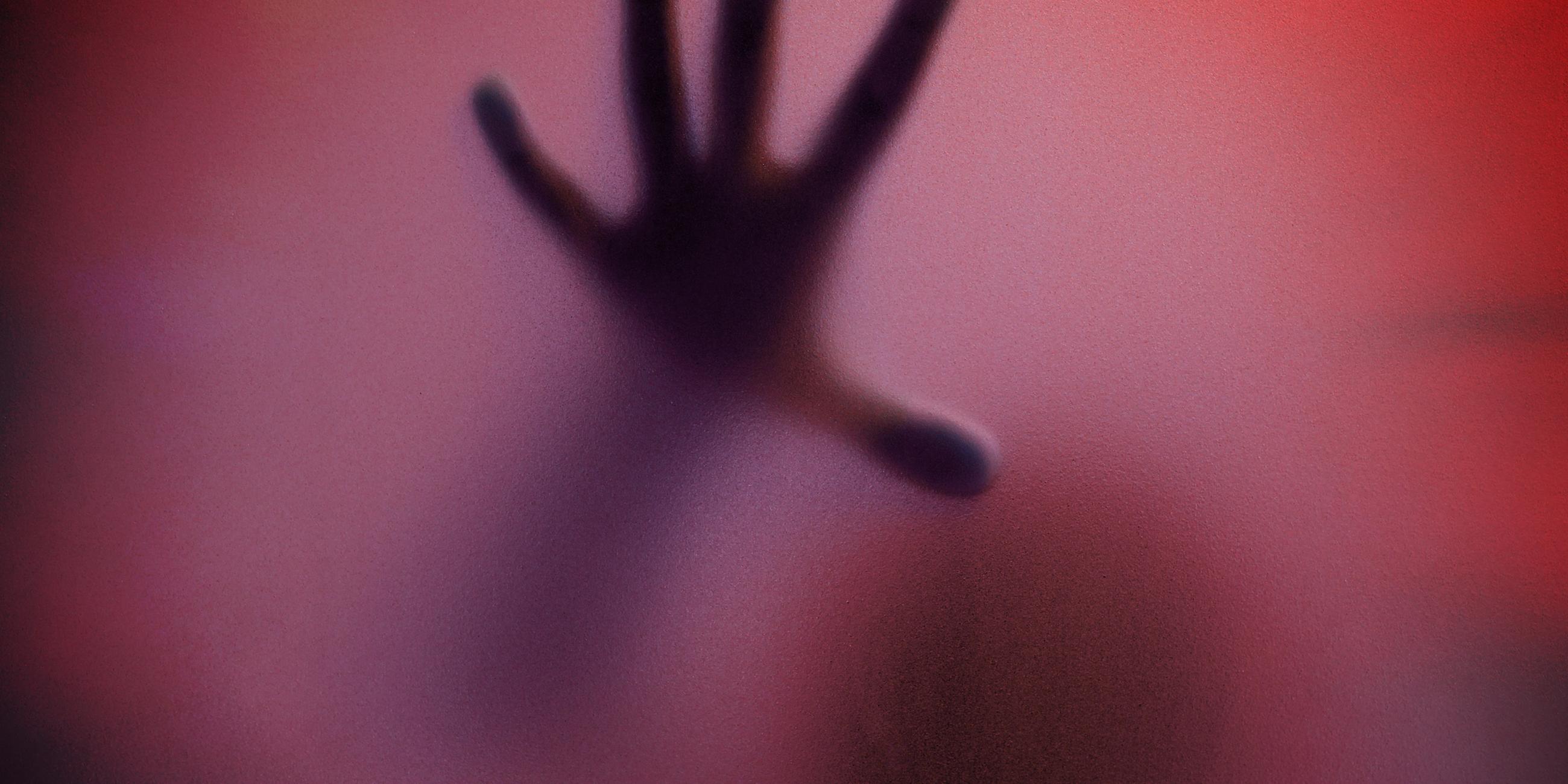 Schatten eines Menschen durch eine matte Glasscheibe in Rottöne getaucht