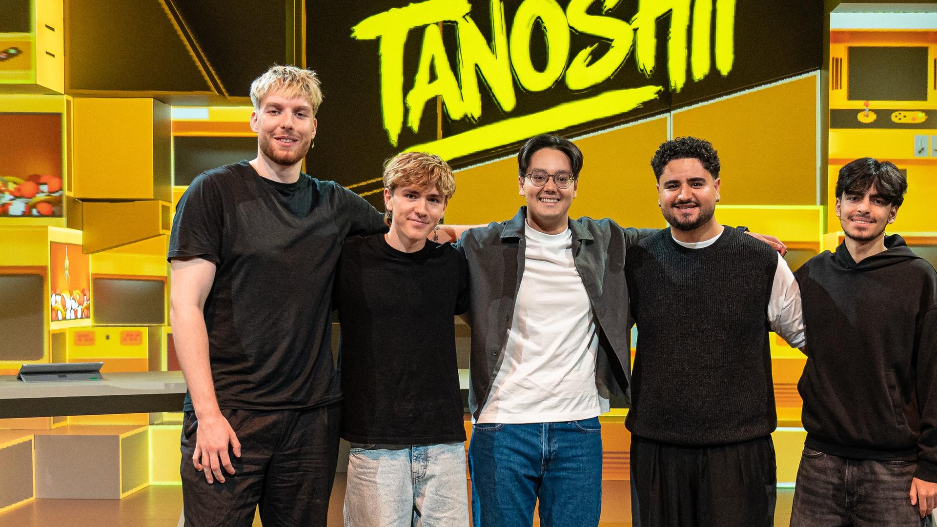 Tanoshii: Die Creators Anigents, Louis, Musa und Azizkazama stehen Arm in Arm im Tanoshii-Studio. In ihrer Mitte steht der Moderator der Sendung, Raafey.