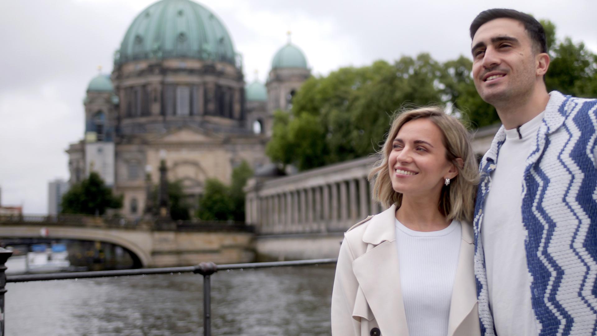 Anna und Anas stehen Arm in Arm und lächeln - im Hintergrund ist der Berliner Dom zu sehen. 