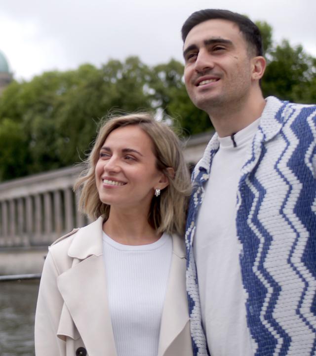 Anna und Anas stehen Arm in Arm und lächeln - im Hintergrund ist der Berliner Dom zu sehen. 