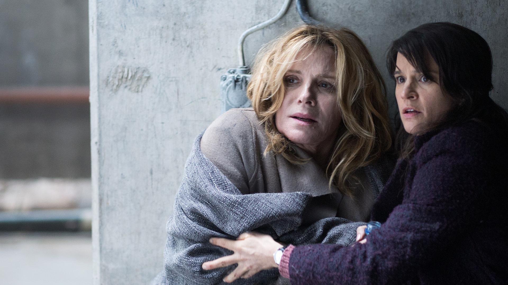 "Anne Holt: Der Mörder in uns": Psychologin Johanne Vik (Melinda Kinnaman) und die amerikanische Präsidentin Helen Tyler (Kim Cattrall) kauern in einer verlassenen Fabrik an einer Säule.