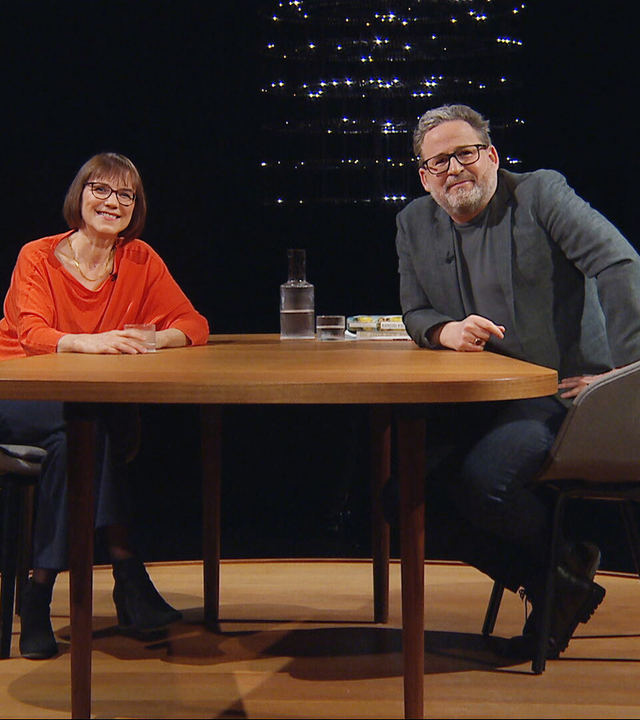 Zwei Personen sitzen sich in einem dunklen Studio an einem Holztisch gegenüber; links Annette Kehnel, rechts Moderator Wolfram Eilenberger.