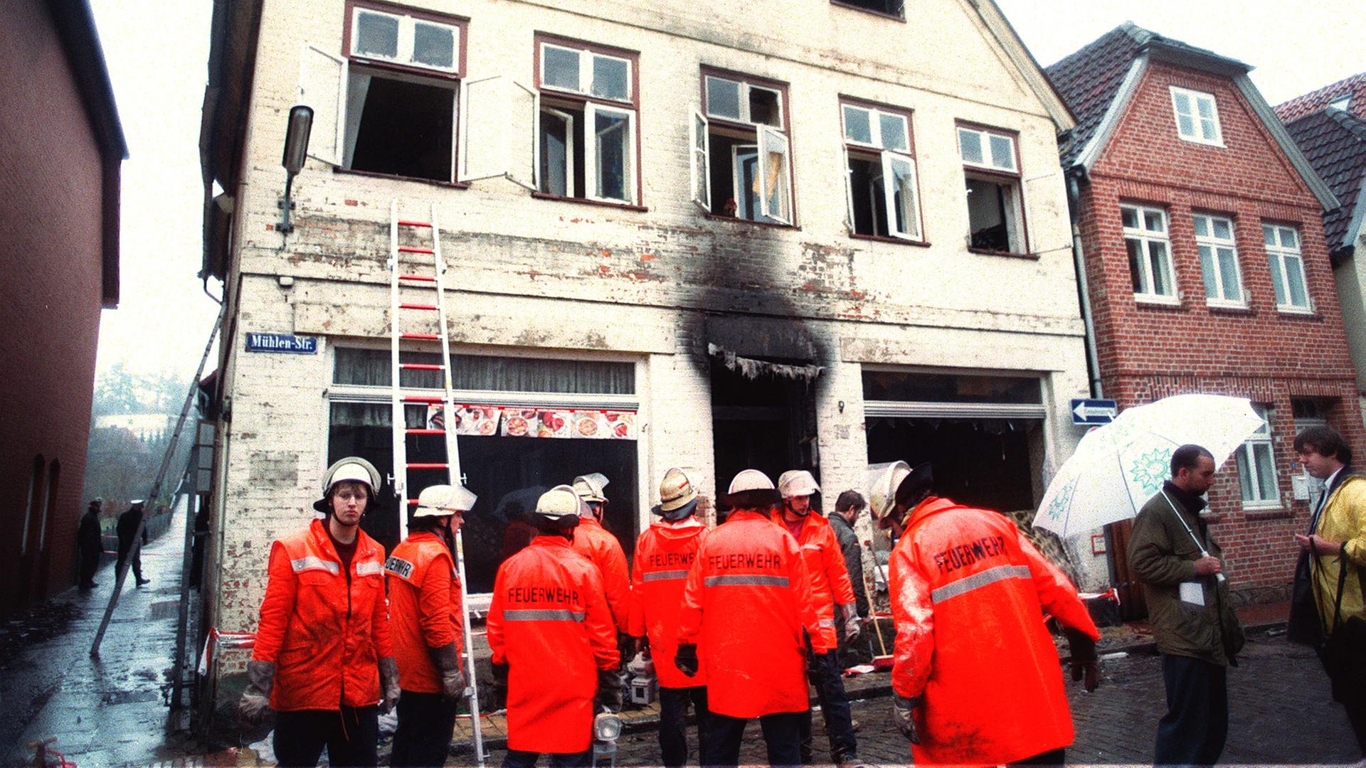 Feuerwehrleute stehen vor einem Haus in Mölln, auf das ein Brandanschlag verübt wurde, 1992