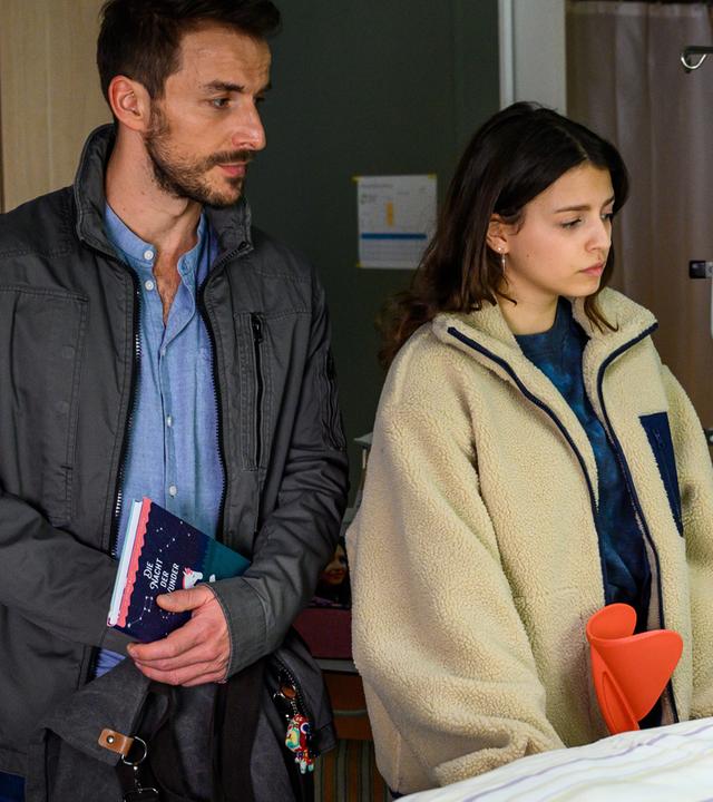 Dr. Frank Stern (Max Alberti) steht mit Emily Hansen (Nina Kaiser) am Krankenbett von ihrer Mutter Paula Hansen (Maya Henselek), die im Koma liegt. Emily und Dr. Stern schauen besorgt auf die Patientin.