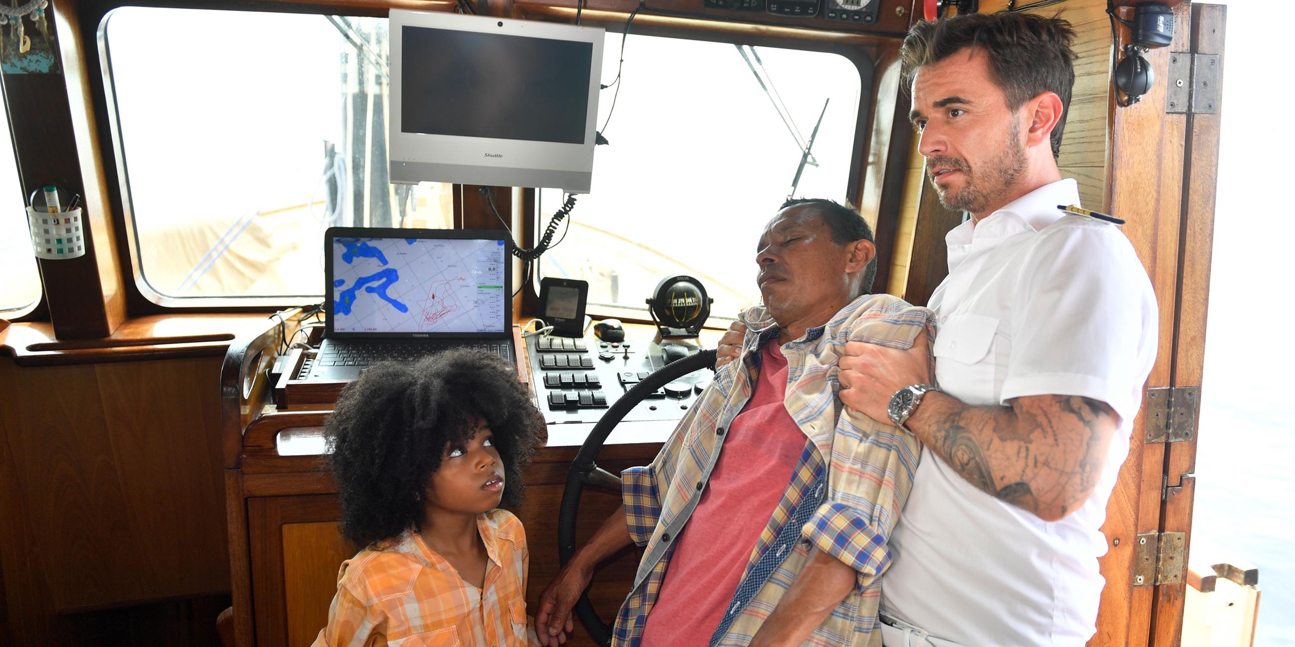 Der kleine Juan (Jordi Ortega) schaut besorgt zu Kapitän Max Pager (Florian Silbereisen), der den bewusstlosen Hernan (Carlos Cardoze) im Arm hält. 