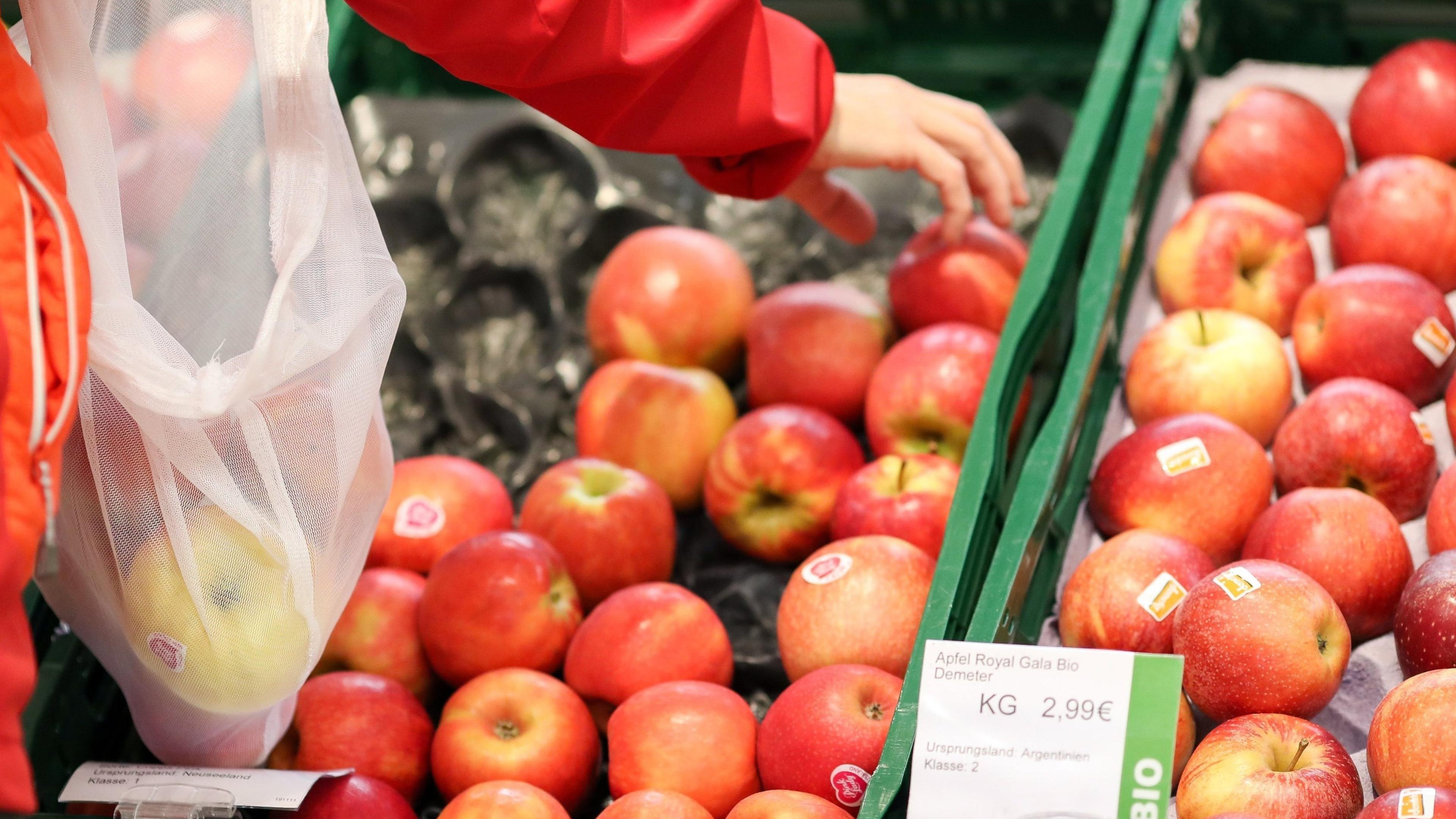 Eine Frau nimmt Äpfel aus einem Supermarktregal und legt sie in ein Frischenetz