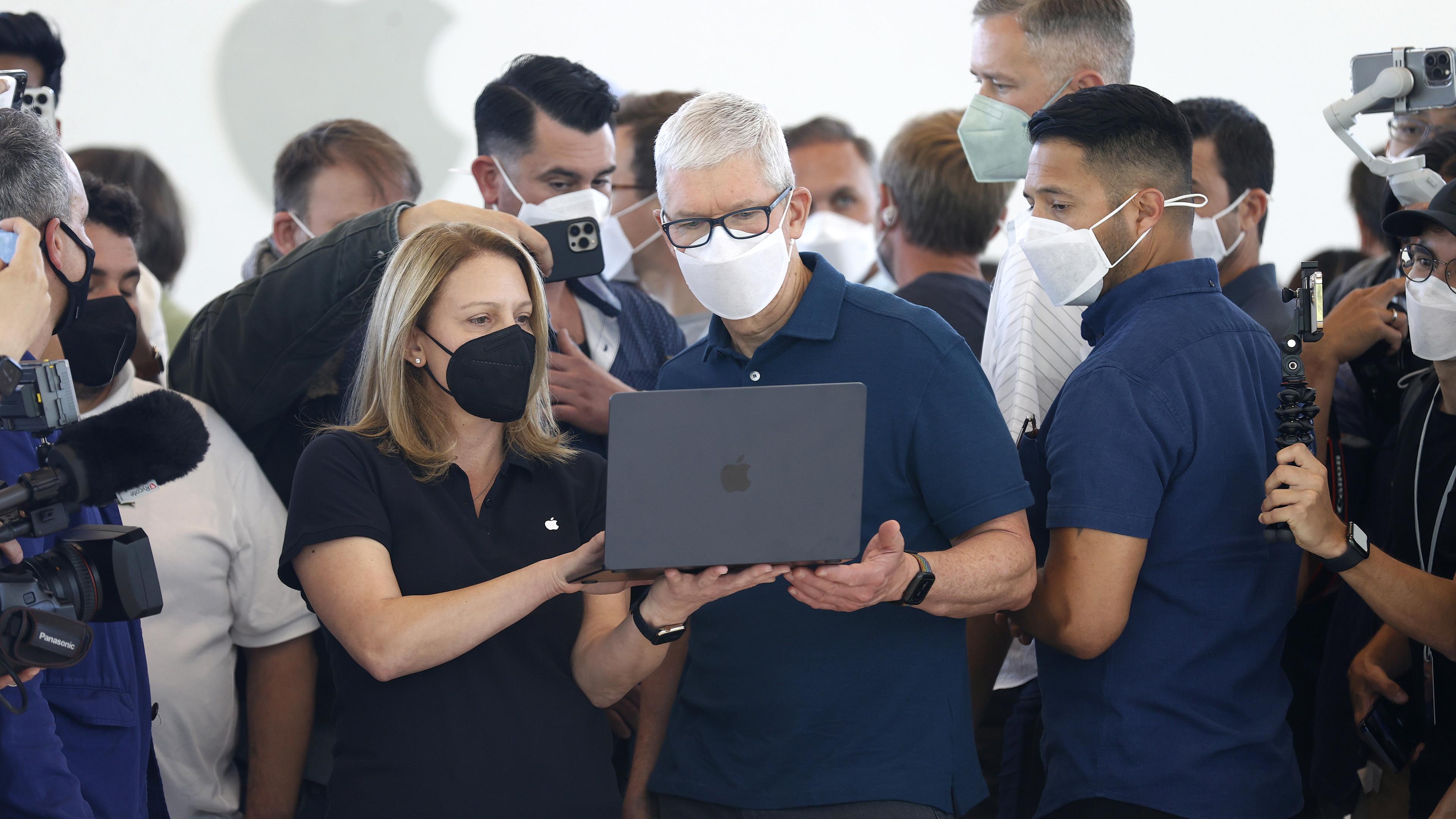 Apple-Chef Tim Cook ist von Menschen umringt während er einen Laptop-Computer seines Unternehmens bedient.