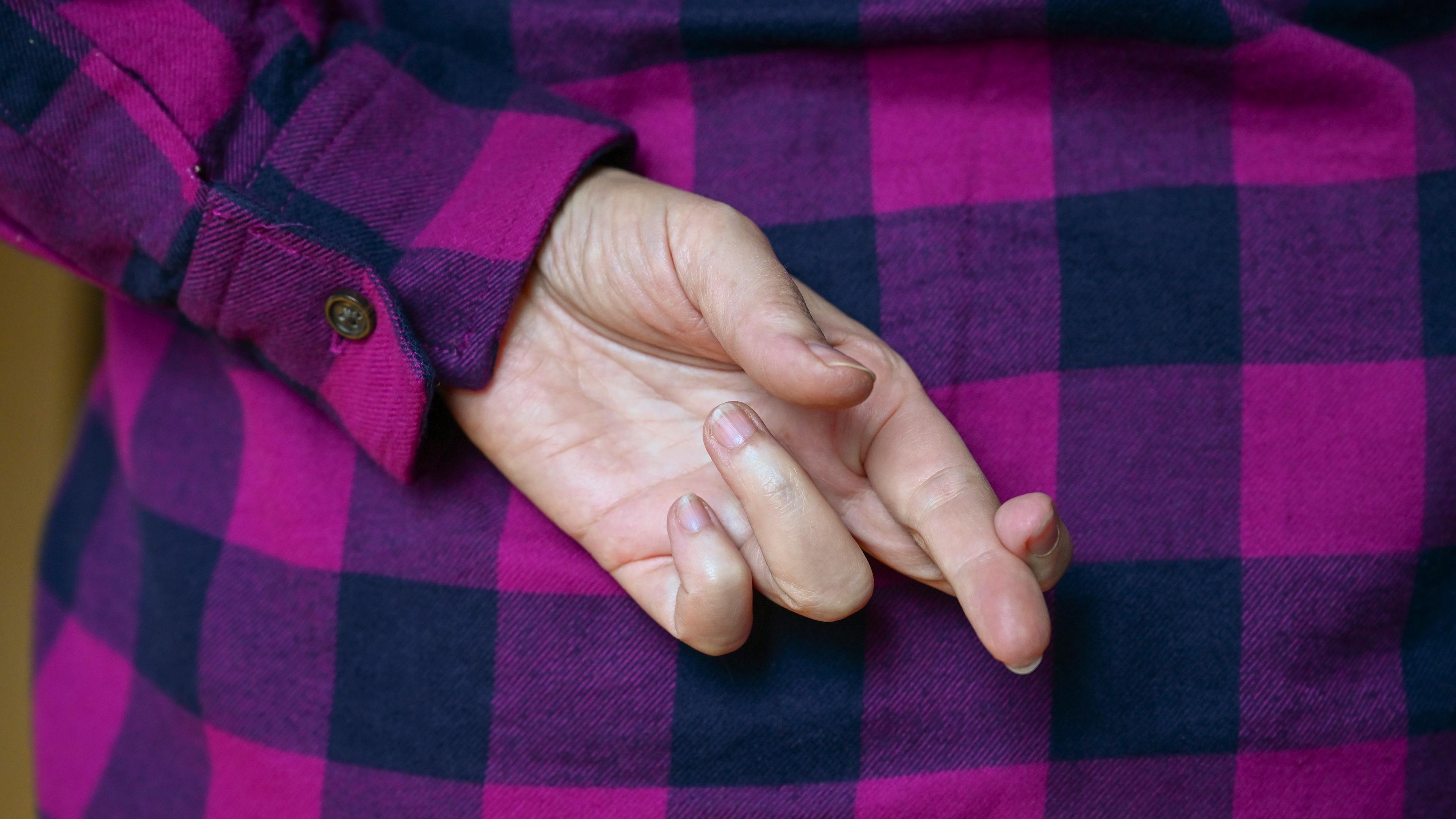 Eine Frau hat hinter ihrem Rücken die Finger gekreuzt.