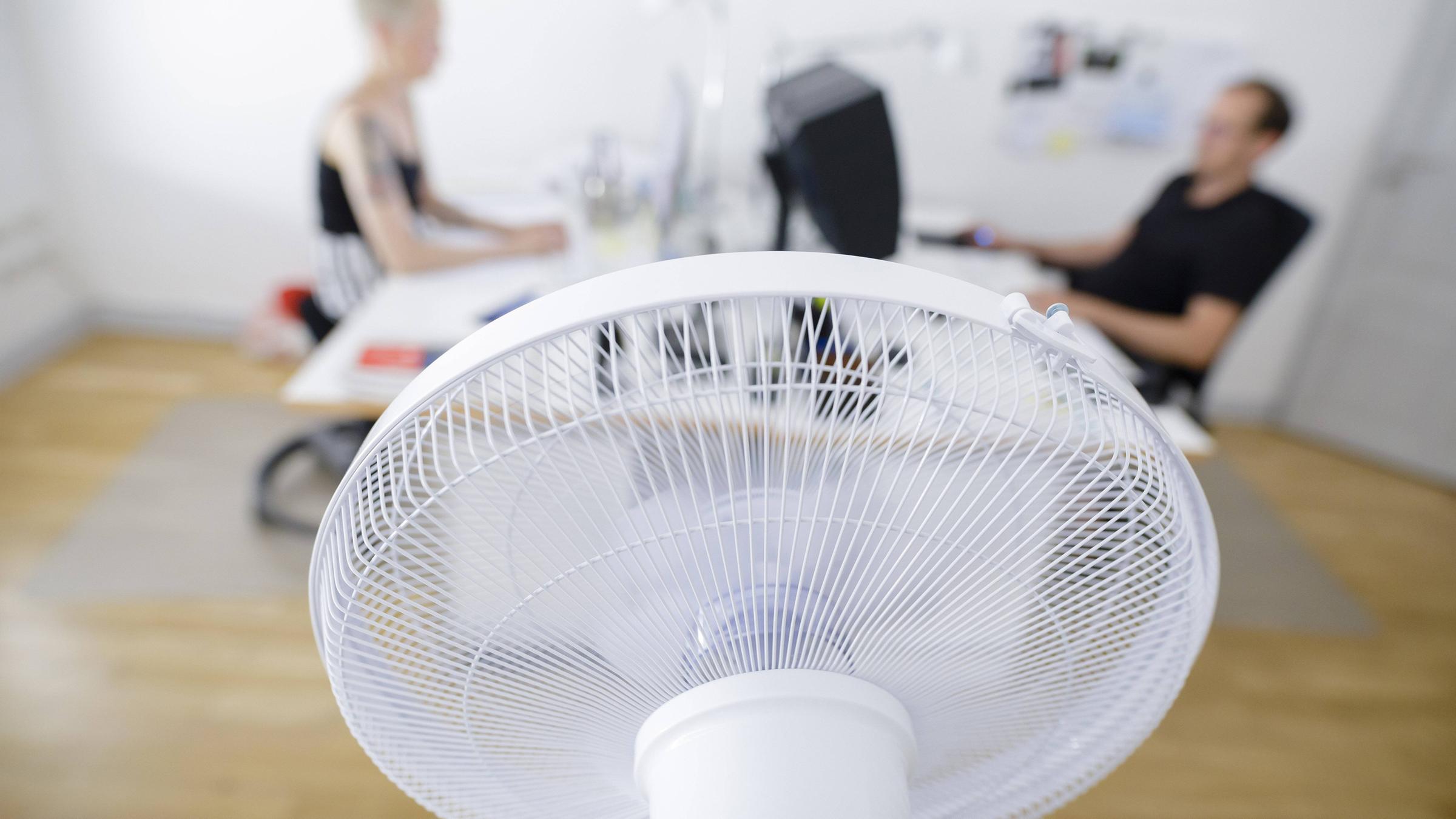 Ein Ventilator dreht vor einem Schreibtisch in einem Büro. 