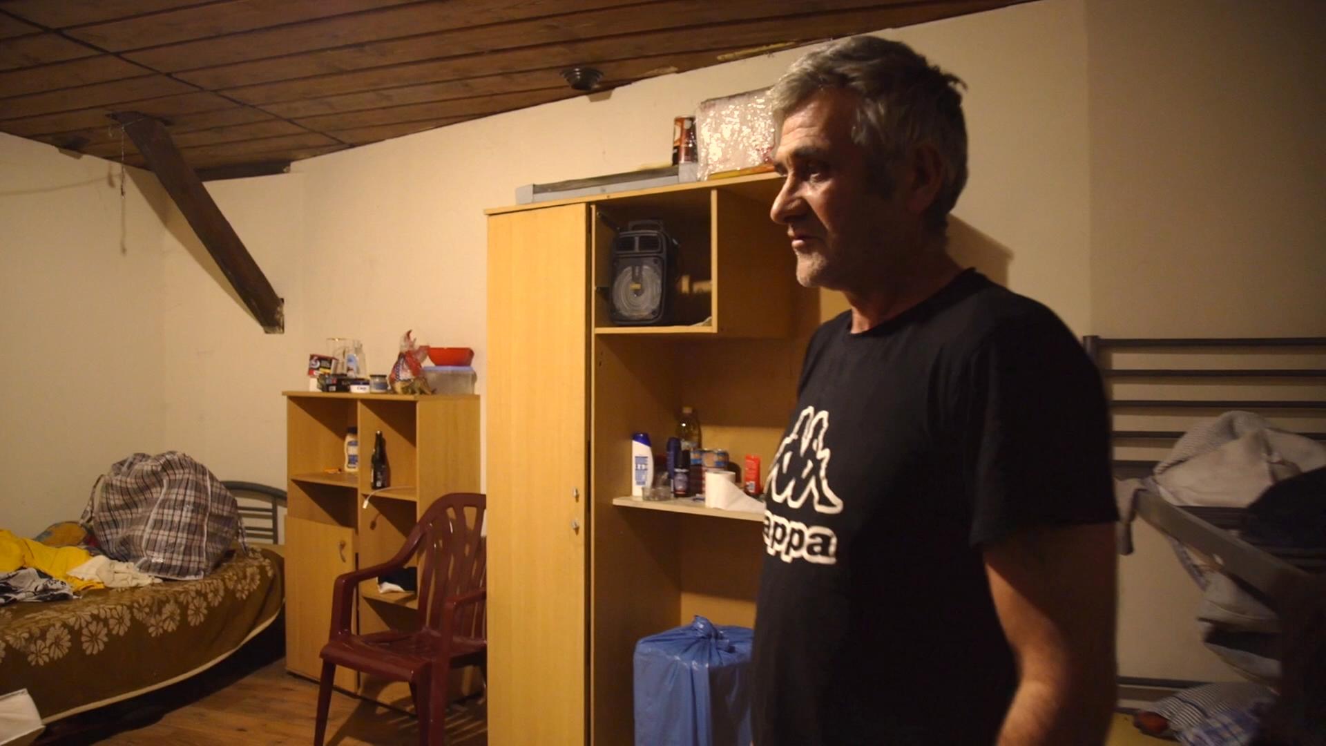 Männliche Arbeitskraft aus Serbien in heruntergekommener Unterkunft bei schummrigem Licht vor Etagenbett und alter Schrankwand