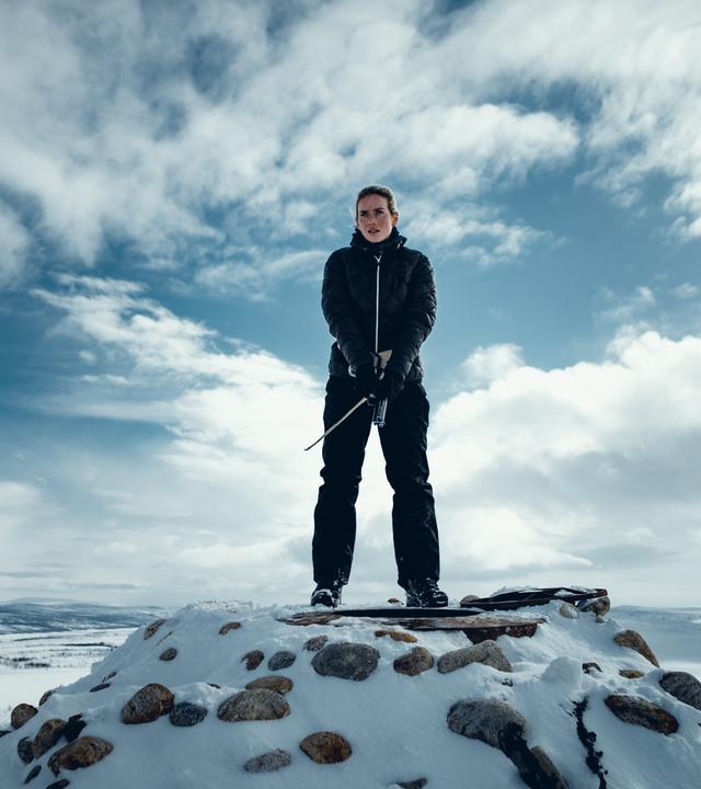 "Arctic Circle - Der unsichtbare Tod (10)": Nina Kautsalo (Iina Kuustonen) steht auf einem schneebedeckten Berg. Über ihr am Himmel sieht man Wolkenformationen.