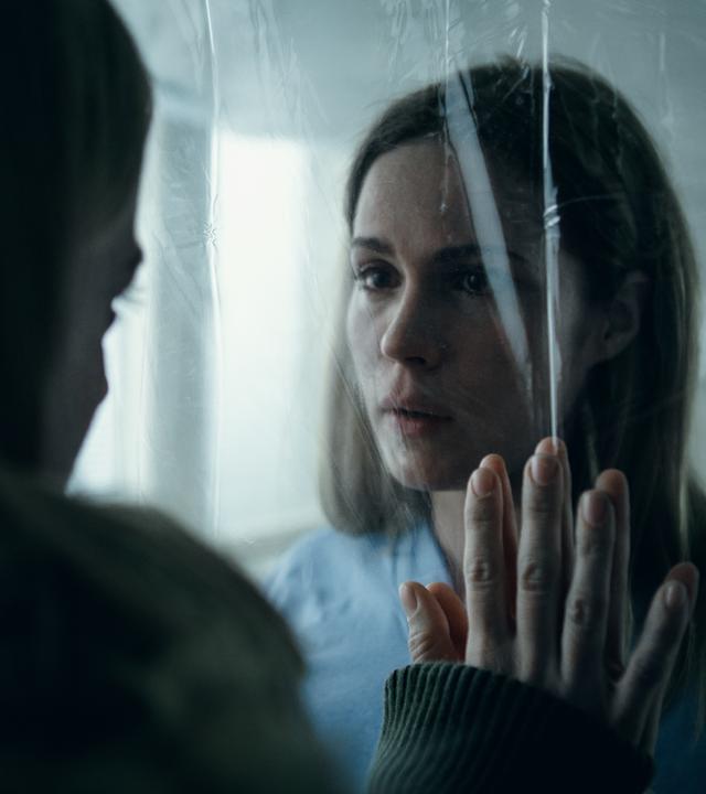 "Arctic Circle - Der unsichtbare Tod (8)": Nina Kautsalo (Iina Kuustonen) - von hinten zu sehen - und ihre Schwester Marita (Pihla Viitala) stehen sich in ihrem Krankenhauszimmer gegenüber. Sie wurde in Quarantäne isoliert, die beiden trennt eine durchsichtige Plane.
