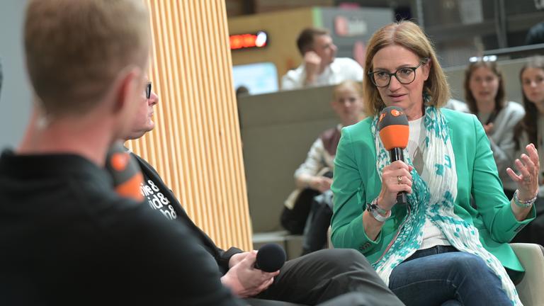 Bettina Schausten mit Mikrofon neben anderen Gästen auf dem Podium der "ARD ZDF Media Stage" auf der re:publica25