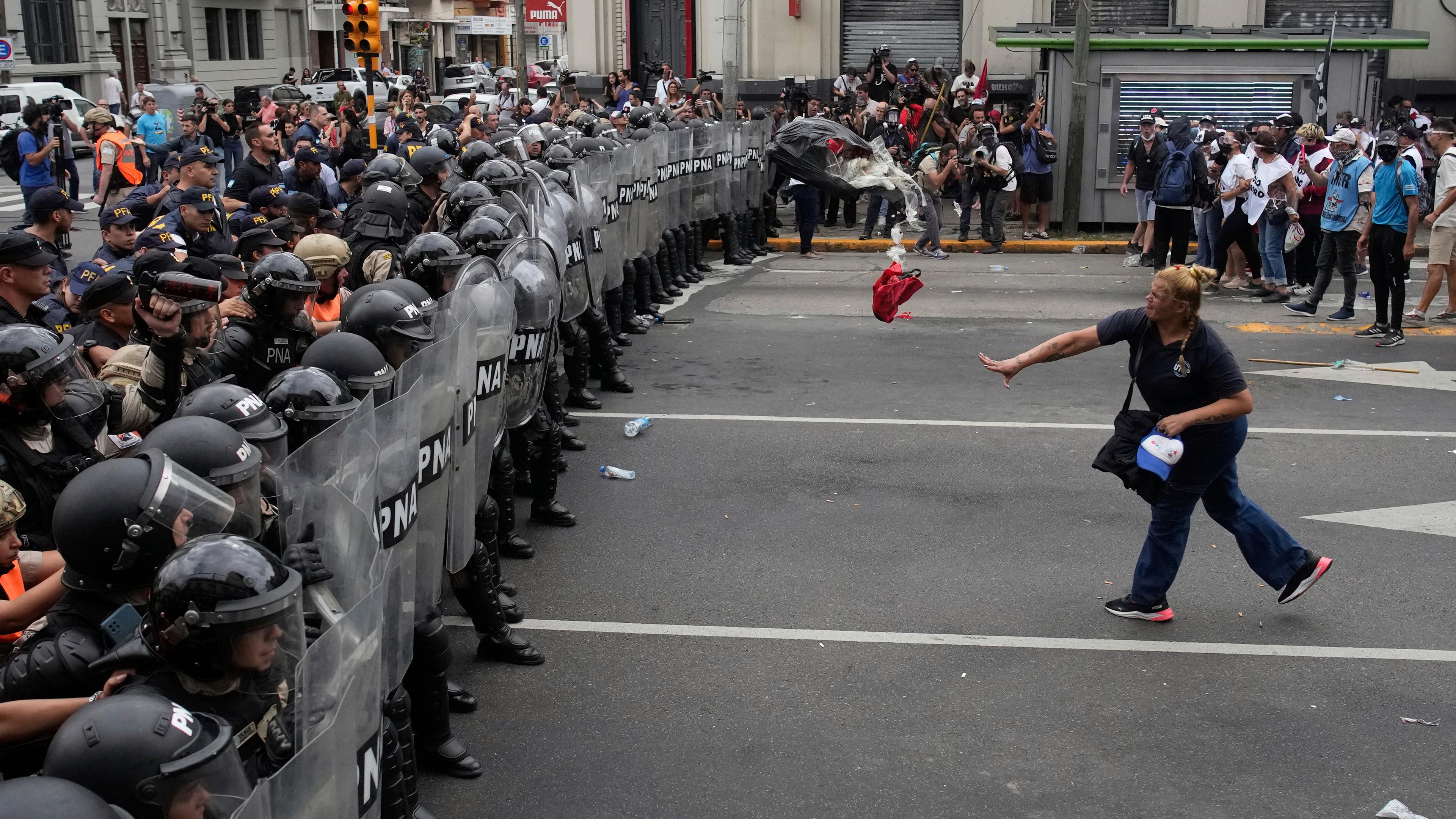 Eine Frau wirft Müll auf eine Wand bewaffneter Polizisten bei Protesten in Argentinien.