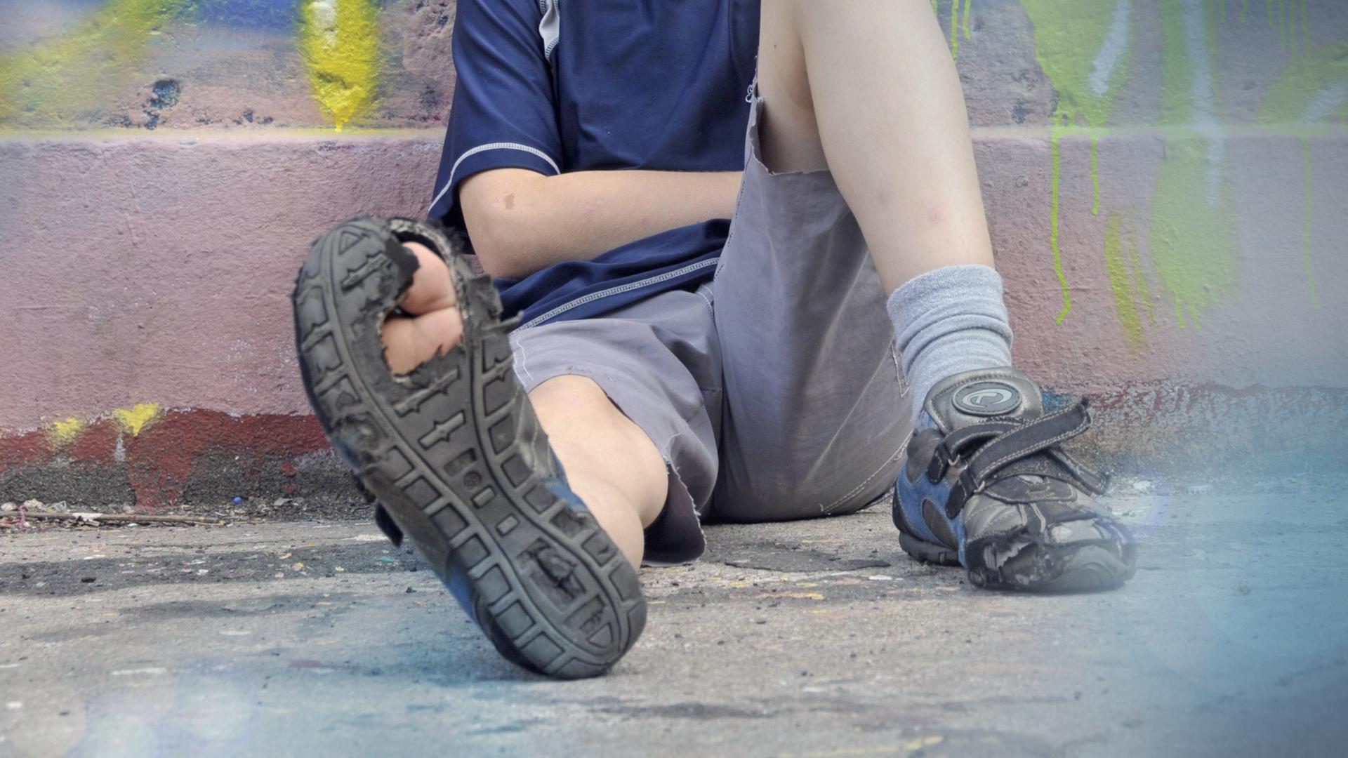 Junge mit kaputtem Schuh sitzt auf einer Strasse