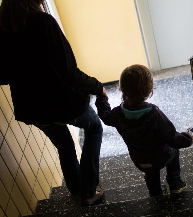 Gegenlicht: Mutter geht mit ihrem Kind die Treppe runter in einem Sozialbau