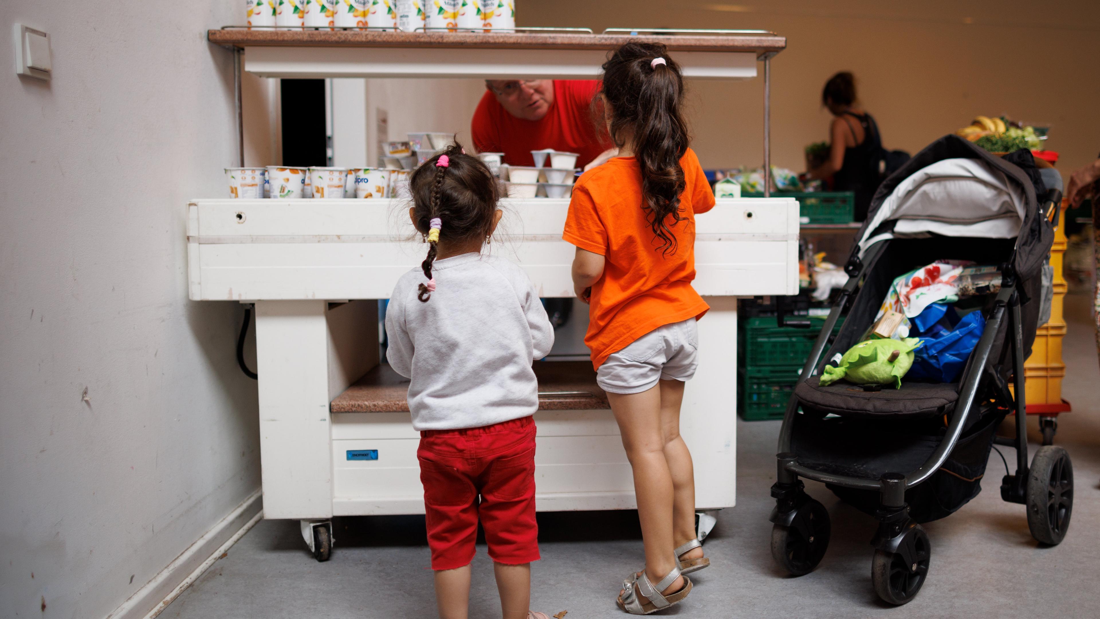 Ein Mitarbeiter verteilt Jogurt an zwei Kinder in der Ausgabestelle Paul-Schneider-Haus der Berliner Tafel.