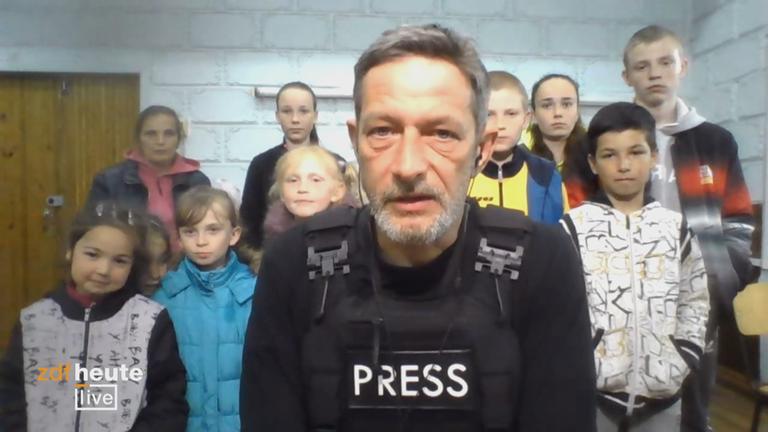 Reporter Arndt Ginzel mit Kindern im Hintergrund. ZDFheute live Logo unten links.