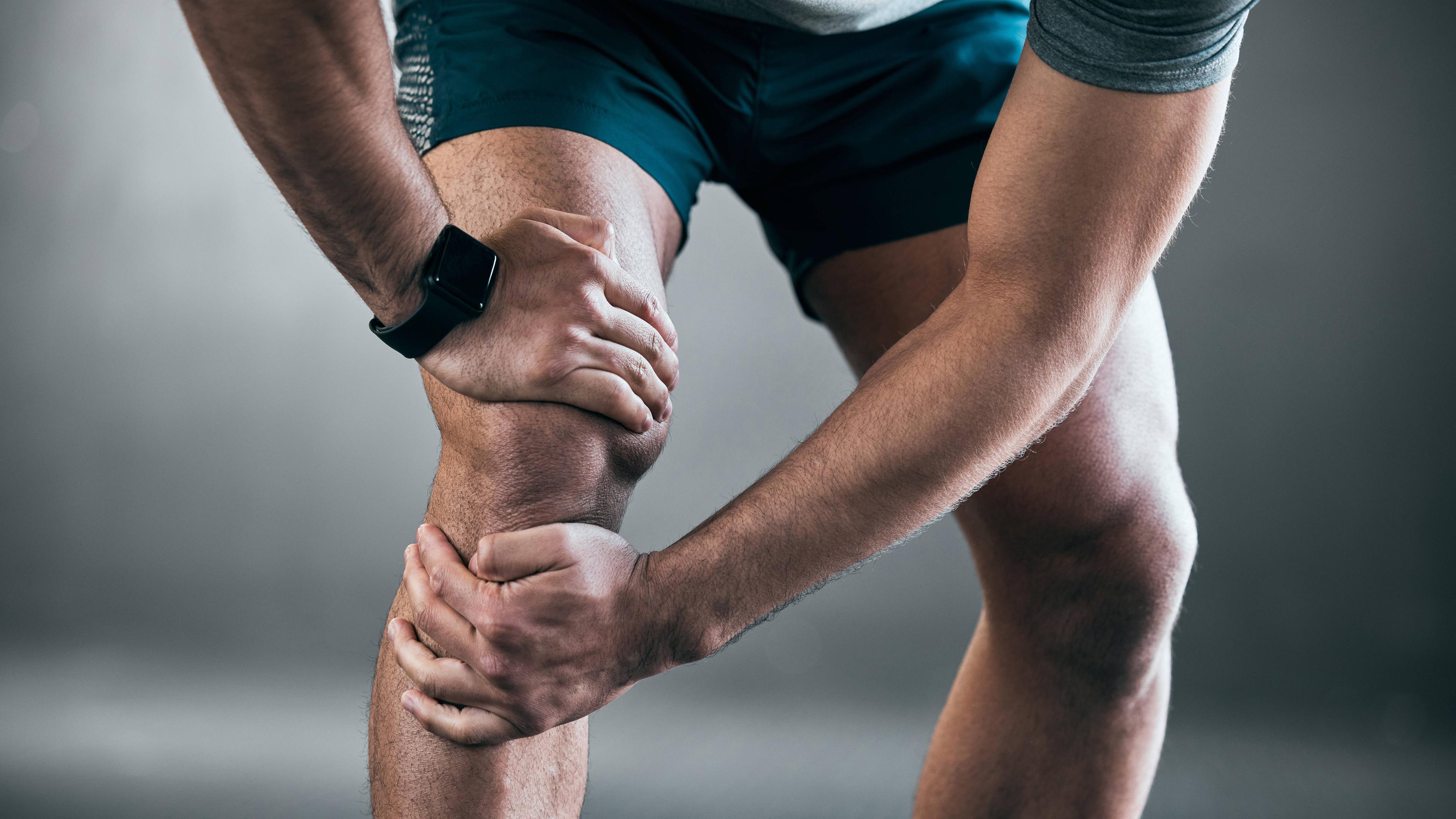 Ein Sportler hält sich vor einem grauen Hintergrund sein Knie vor Schmerzen, aufgenommen am 12.02.2023