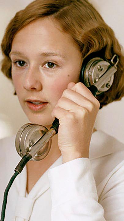 Astrid (Alba August) telefoniert mit einem antiken Telefon, das an der Wand hängt.