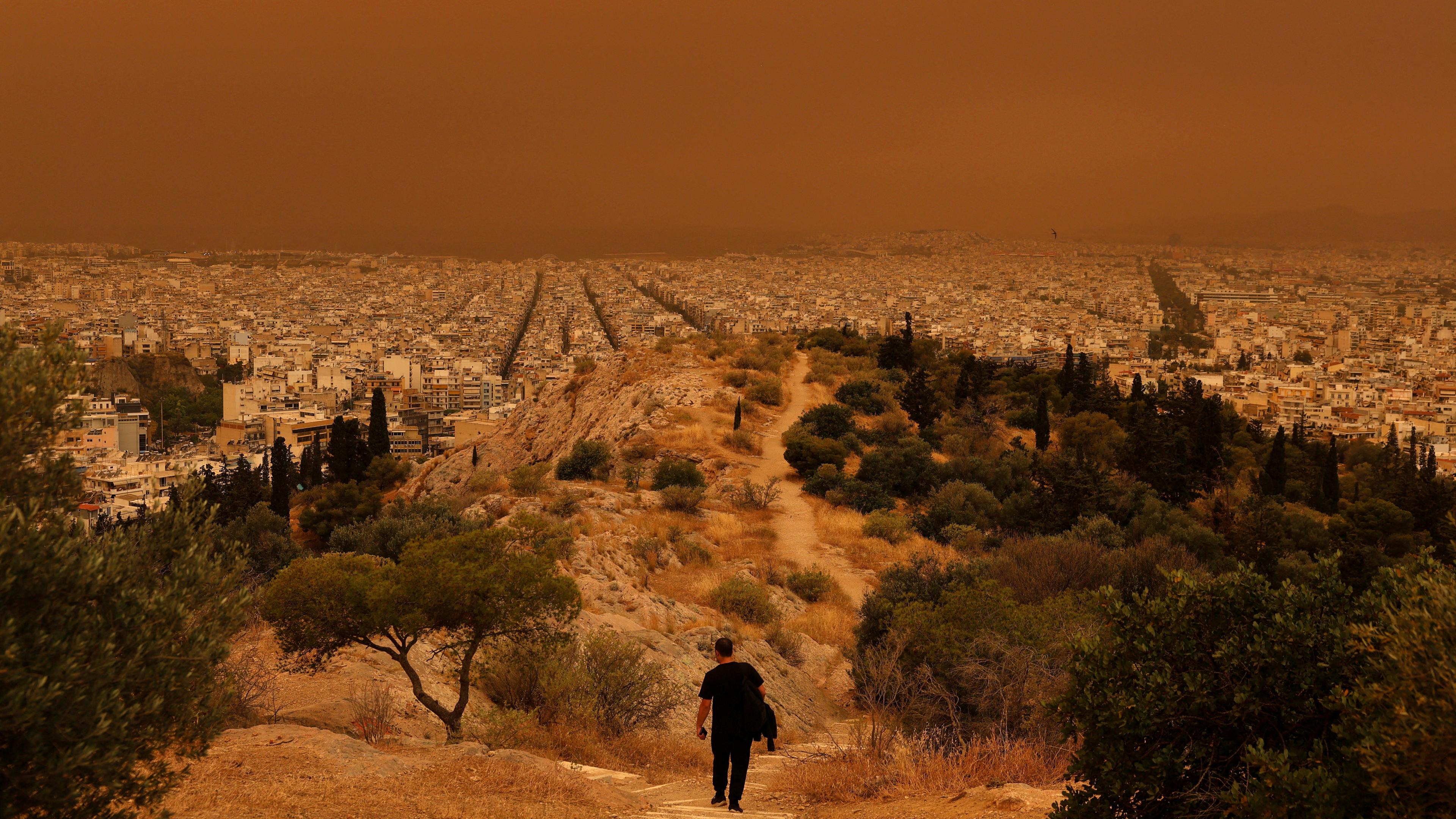 Ein Mann macht sich auf den Weg zu einem Hügel, während afrikanischer Staub aus der Wüste Sahara die Stadt Athen in Griechenland bedeckt