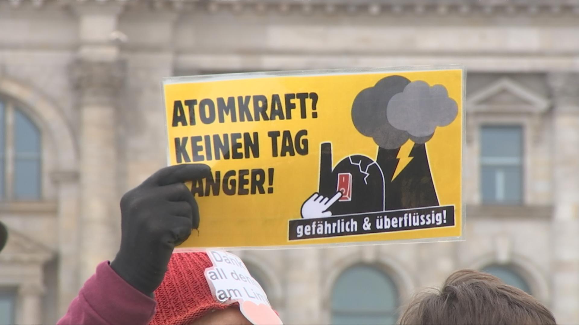 Atomkraftgegner hält ein Schild hoch, auf dem ein Atomkraftwerk zu sehen ist, mit dem Slogan "Atomkraft? Keinen Tag länger!"