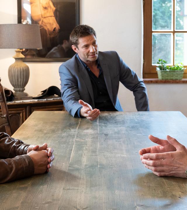 Kommissar Kaya (Baran Hêvî), Kommissar Hansen (Igor Jeftić) und Gabriel Schneider sitzen an einem gescheuerten Holztisch in einem Wohnraum und unterhalten sich. Im Hintergrund ist eine Tischlampe auf einer Kommode zu sehen sowie ein Pferdeporträt an der Wand.