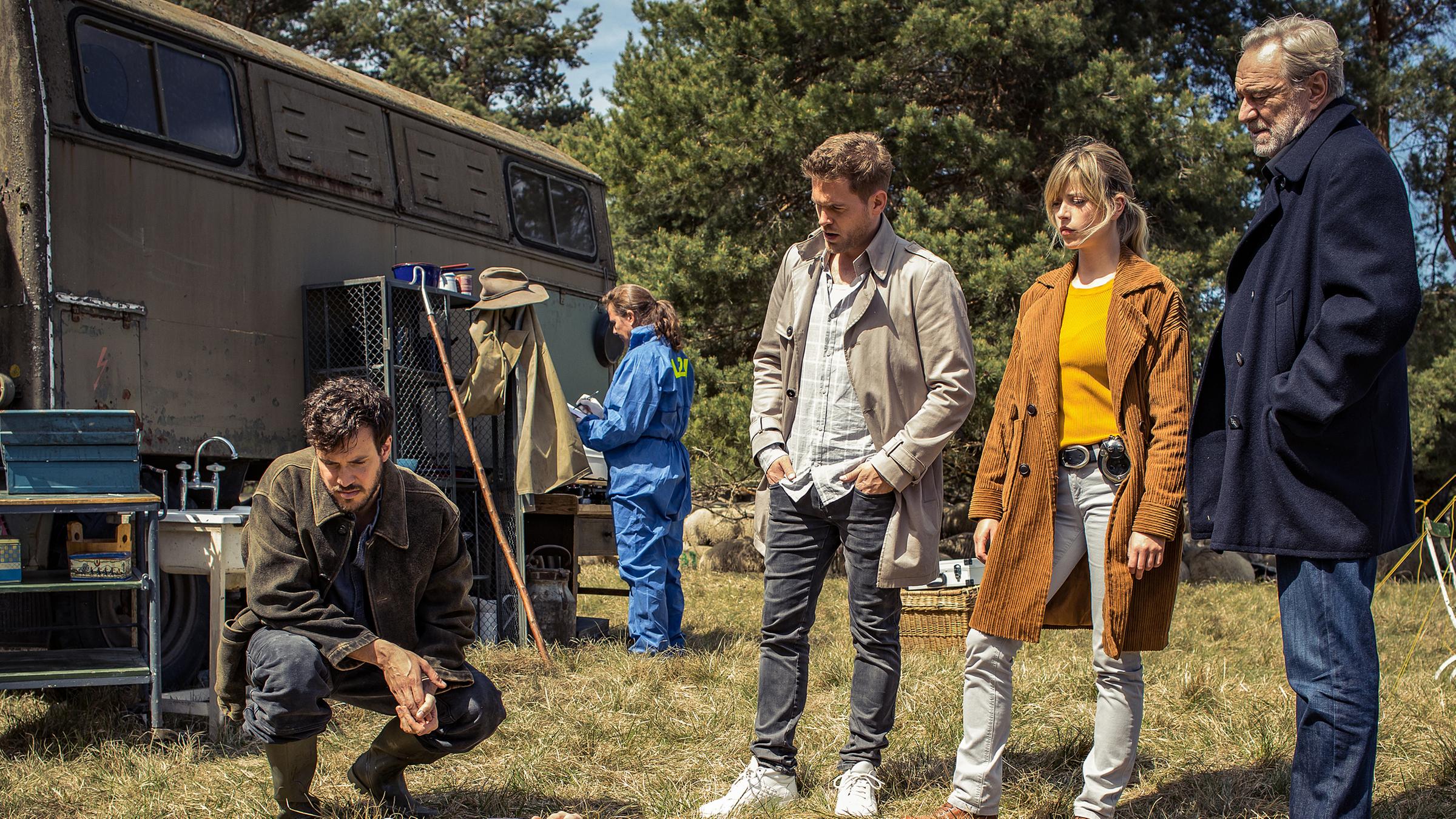 Die Kommissare Resi Schwaiger (Mersiha Husagic), Arthur Bauer (Gerd Silberbauer) und Dominik Morgenstern (Joscha Kiefer) stehen am Tatort hinter der Leiche. Sie beobachten, Ben Michaelis (Tobias van Dieken), ein Mitarbeiter des Opfers, wie er neben dem Opfer in Hocke geht und es betrachtet. Im Hintergrund ist der Wohnwagen des Schäfers und die Spurensicherung (Komparsen) zu sehen. Es ist ein sonniger Tag.
