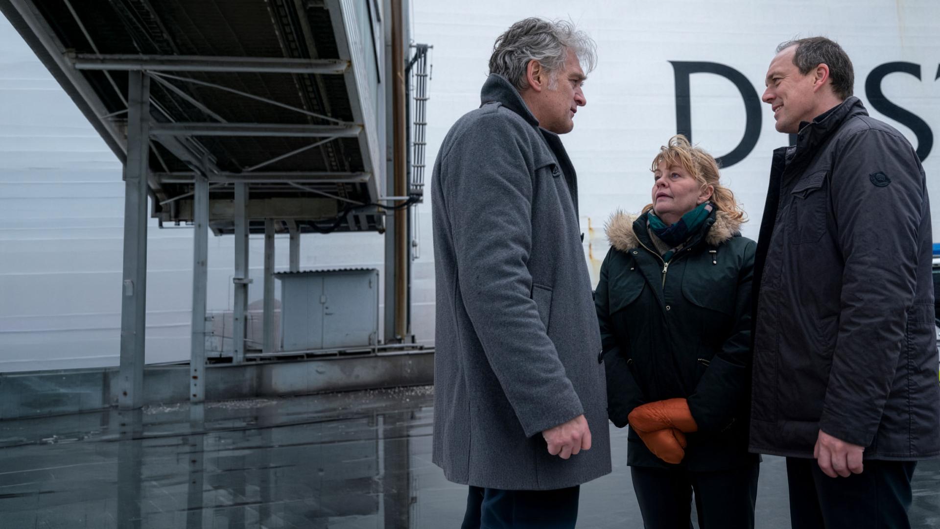 "Der Kommissar und das Meer - Auf dunkler See": Robert (Walter Sittler), Ewa (Inger Nilsson) und Thomas (Andy Gätjen) stehen sich freundlich zugewandt im Kreis. im Hintergrund ein Polizeiwagen sowie eine Fähre.