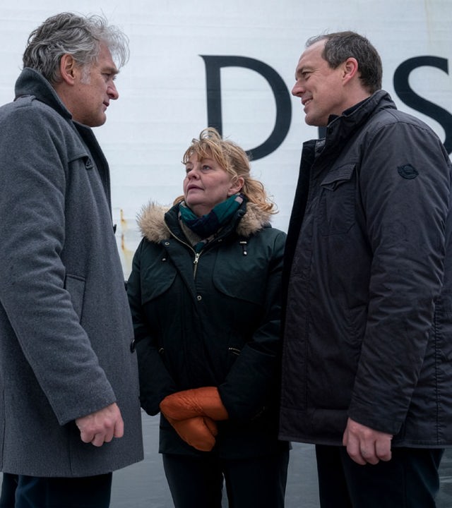 "Der Kommissar und das Meer - Auf dunkler See": Robert (Walter Sittler), Ewa (Inger Nilsson) und Thomas (Andy Gätjen) stehen sich freundlich zugewandt im Kreis. im Hintergrund ein Polizeiwagen sowie eine Fähre.