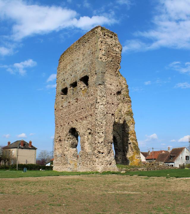 Antike Ruine des Janus-Tempel in Autun bestehend aus den Überresten zweier Wände auf freiem Feld. Im Hintergrund einzelne moderne Wohnhäuser.