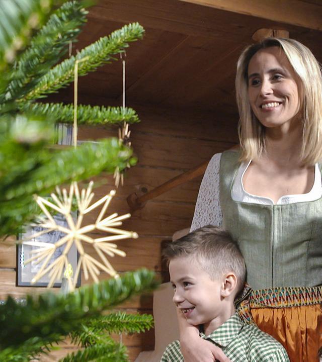 Mutter mit zwei Kindern lächelnd vor einem Weihnachtsbaum