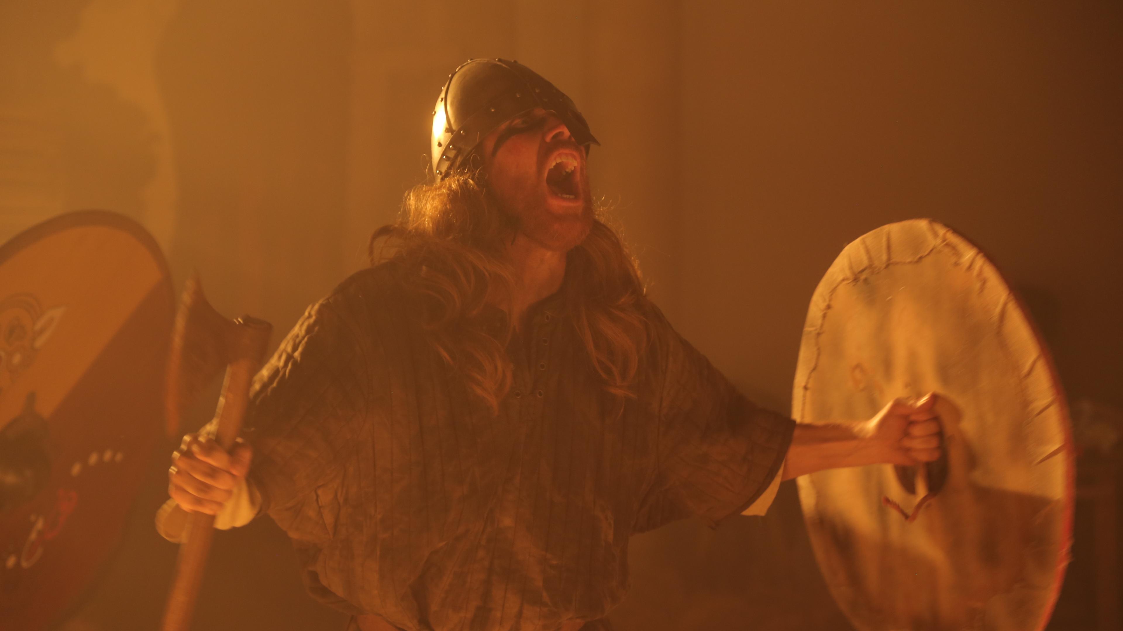 "Aufgedeckt: Das Geheimnis des Wikingergrabs": Spielszene: Ein Mann mit Helm schreit aus vollem Hals. Er hält in der einen Hand ein rundes Schild, in der anderen eine Axt.