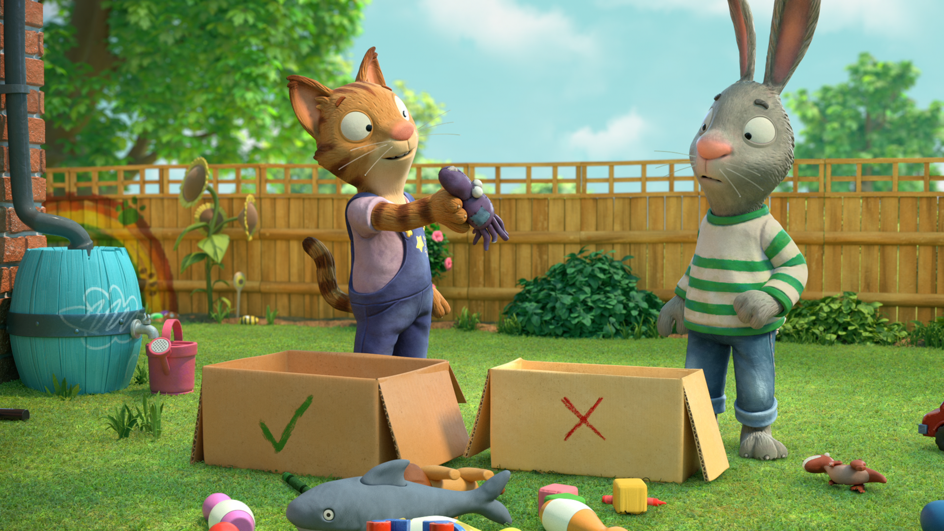 Frankie zeigt Pip im Garten ein altes Spielzeug. Pip überlegt, ob er es behalten oder wegwerfen möchte. Vor ihnen steht jeweils ein Pappkarton zum Ausmisten.