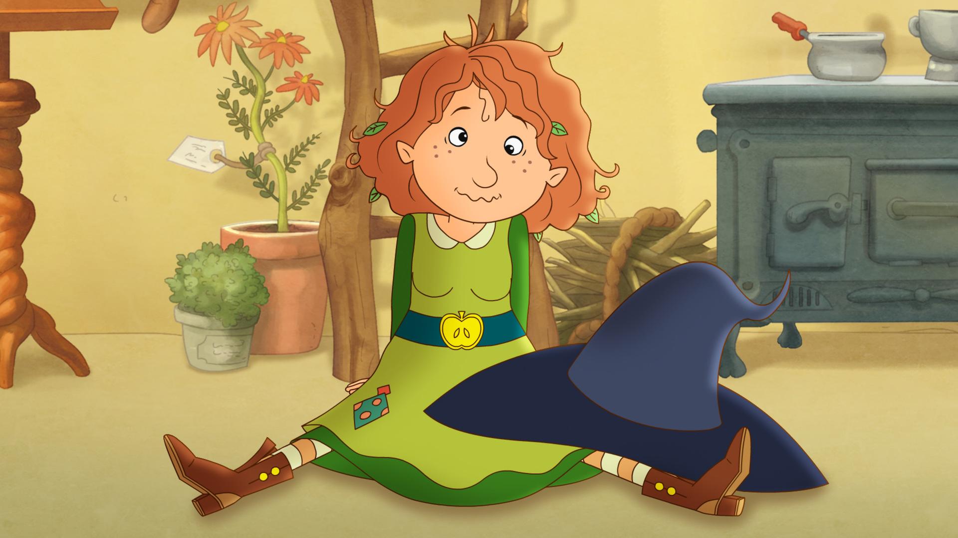 Petronella sitzt schielend auf dem Boden, auf ihren Knien der Hexenhut.