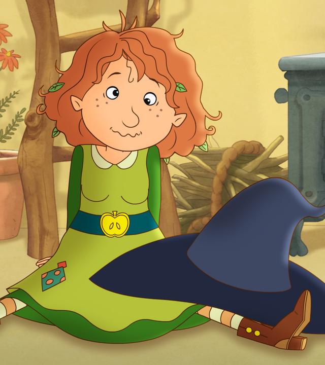 Petronella sitzt schielend auf dem Boden, auf ihren Knien der Hexenhut.