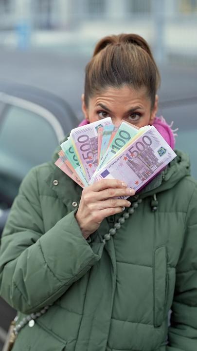 Katty Salié vor einer Limousine mit Geldscheinen in der Hand