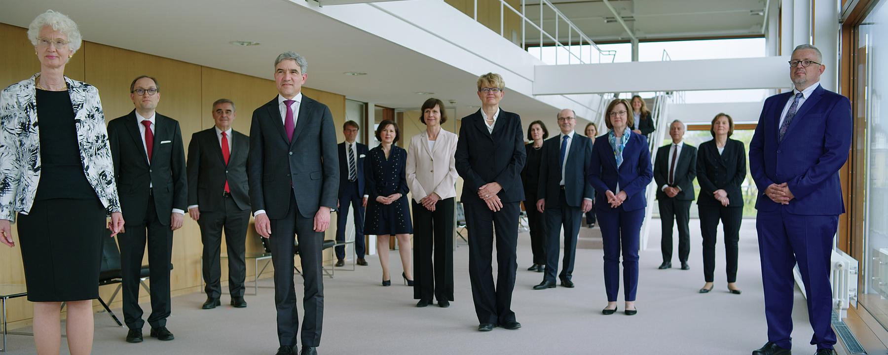 Die 16 Richter*innen des Bundesverfassungsgerichts stehen im Foyer des Sitzungssaals und schauen in die Kamera.