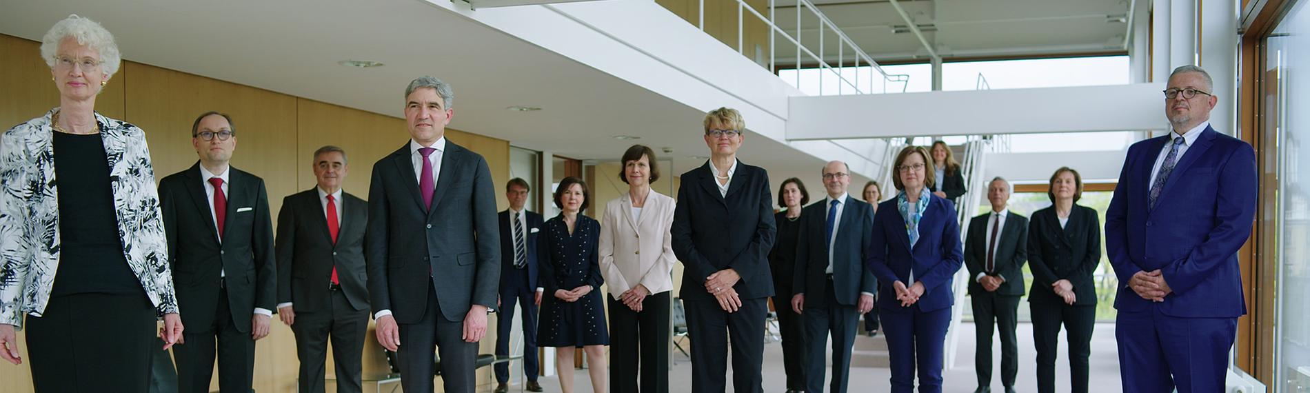 Die 16 Richter*innen des Bundesverfassungsgerichts stehen im Foyer des Sitzungssaals und schauen in die Kamera.