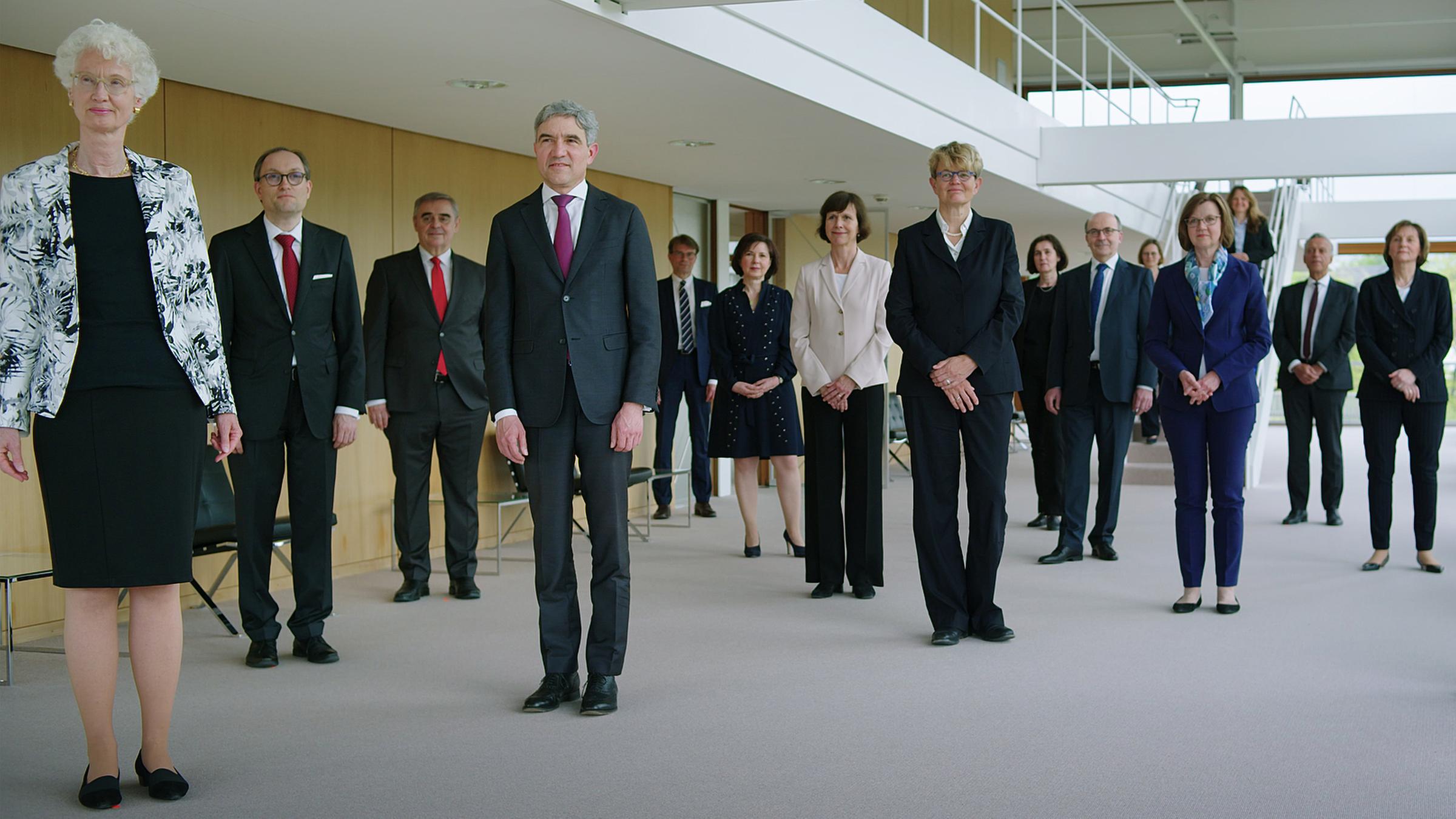 Die 16 Richter*innen des Bundesverfassungsgerichts stehen im Foyer des Sitzungssaals und schauen in die Kamera.