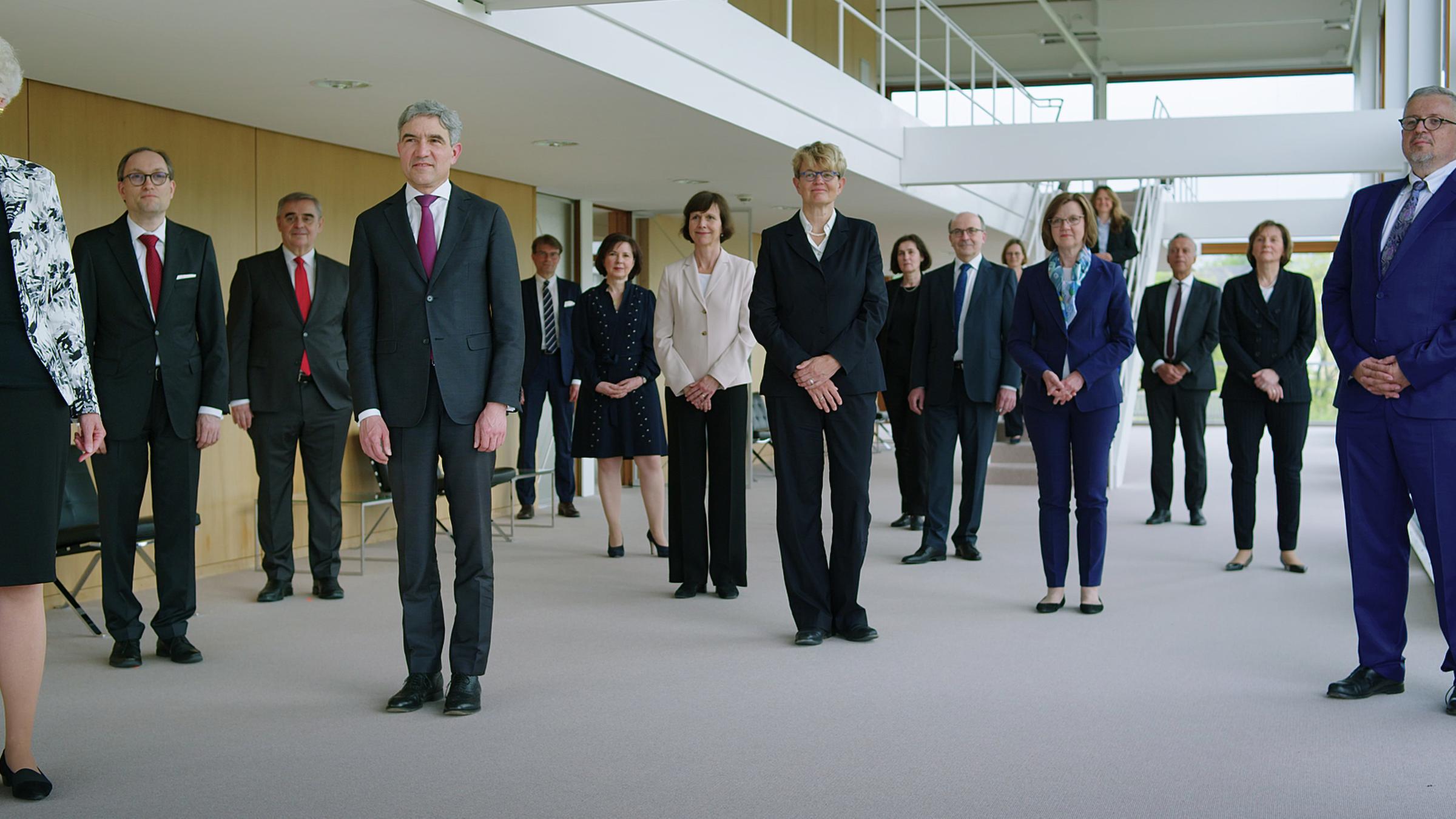 "Auftrag Gerechtigkeit - Wieviel Macht hat das Bundesverfassungsgericht?": Die 16 Richter*innen des Bundesverfassungsgerichts stehen im Foyer des Sitzungssaals und schauen in die Kamera.