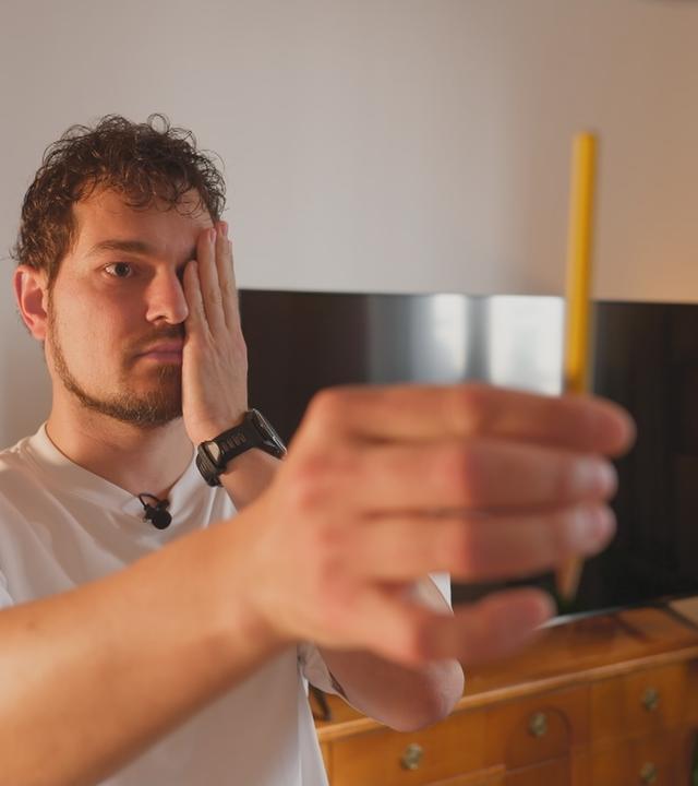 Mann hält sich ein Auge zu und schaut auf einem Stift in der anderen ausgestreckten Hand.