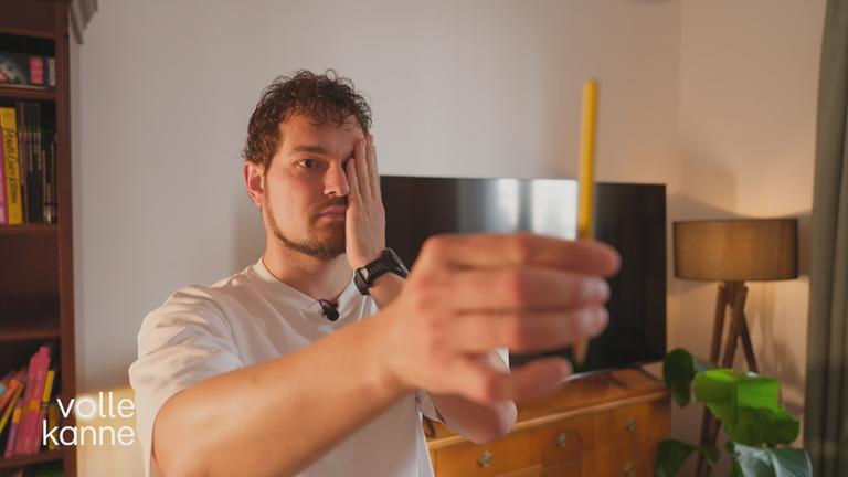 Mann hält sich ein Auge zu und schaut auf einem Stift in der anderen ausgestreckten Hand.