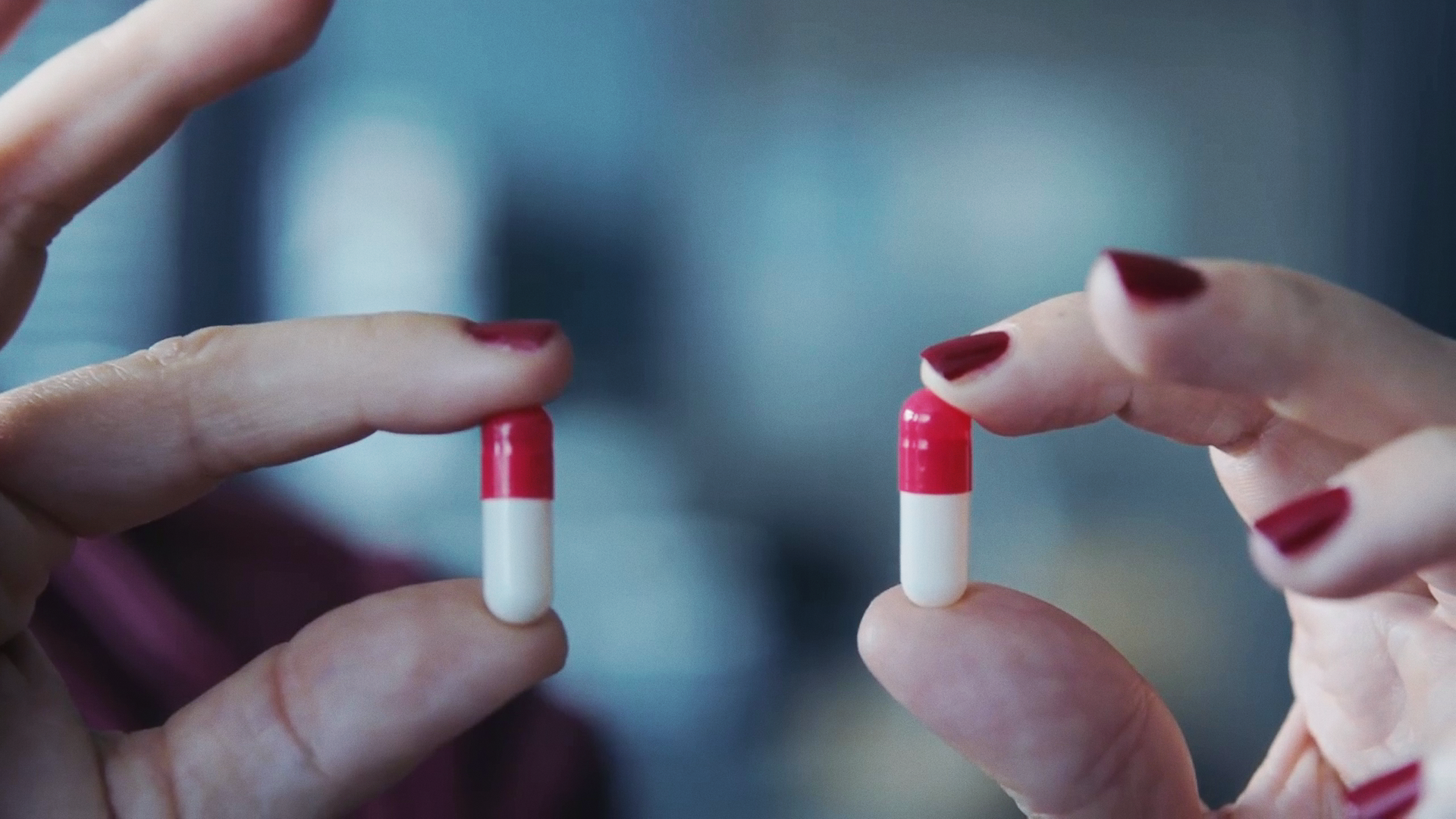 Zwei Hände mit lackierten Fingernägeln halten zwei Tabletten zwischen Daumen und Zeigefinger. 