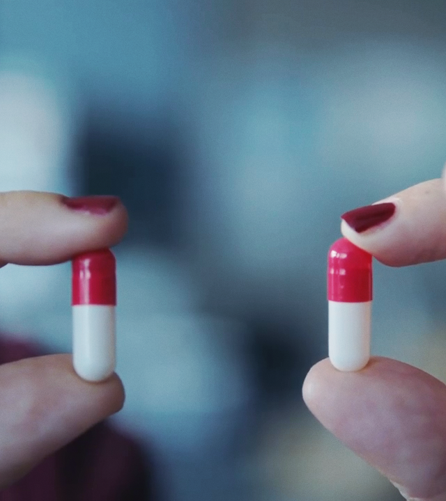Zwei Hände mit lackierten Fingernägeln halten zwei Tabletten zwischen Daumen und Zeigefinger. 